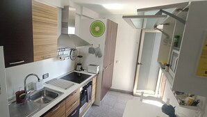 Una cocina compacta con un lavamanos de acero inoxidable, un horno empotrado y un microondas. Hay una ventana pequeña que proporciona luz natural.