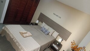 Un dormitorio moderno con una cama grande, dos mesitas de noche, un cabecero montado en la pared y una pieza decorativa en la pared.