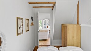 Un pasillo estrecho con una cama a la derecha, vigas de madera en el techo y un armario blanco al fondo.