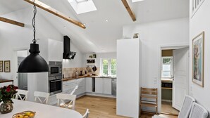 Una cocina moderna con armarios blancos, una lámpara colgante negra y techo de madera.