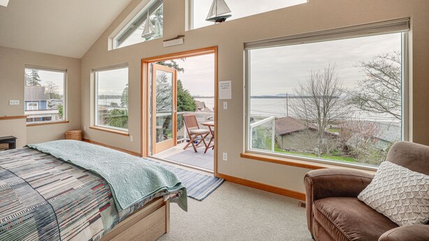 A bedroom with a large window, a bed, a chair, and a view of the outside. - Beautiful Birch Bay Retreat w/ Deck & Fire Pit! (Blaine)