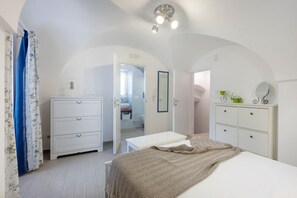 A bedroom with a bed, a dresser, a mirror, and an arched doorway leading to a bathroom.