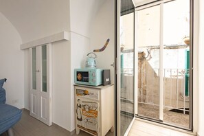 A room with a sliding glass door leading to a balcony, a vintage-style microwave on a cabinet, and a blue chair.