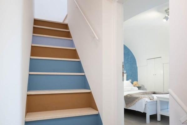 A staircase with alternating brown and blue steps leading to a bedroom with a bed, nightstand, and wardrobe. - WePuglia - Porta Blu (Monopoli)