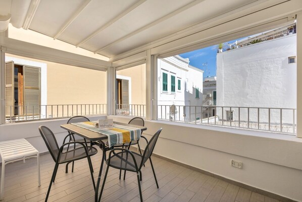 A balcony with a table and chairs, a white railing, and a view of neighboring buildings.