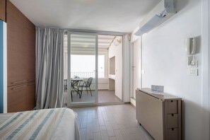 Habitación de hotel con cama, escritorio, silla, puerta corrediza de vidrio a un balcón y un cartel en el escritorio.