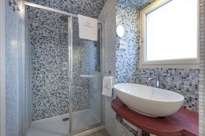 A bathroom with a glass shower enclosure, a white sink, and a tiled backsplash.