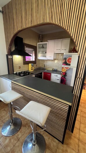 A kitchen with a central island, two bar stools, a stove, a sink, and cabinets.