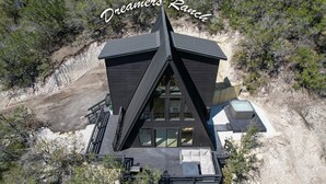 Um edifício moderno com formato triangular, com varanda e área de estar ao ar livre, rodeado por paisagem natural.