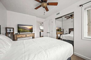 Ein Schlafzimmer mit einem großen Bett, einem Deckenventilator, einem Fernseher und einem Spiegel.