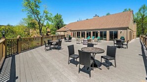 A covered outdoor patio with tables and chairs, a building with a tiled roof, and a wooden deck railing. - Sleeps 4 Mountain Views Indoor Pool & Hot Tub (Gatlinburg)