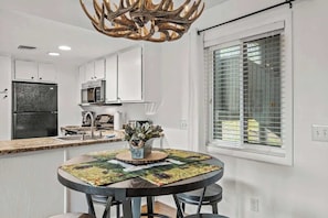 A modern kitchen with white cabinets, a black refrigerator, a microwave, and a dining area with a round table and chairs.