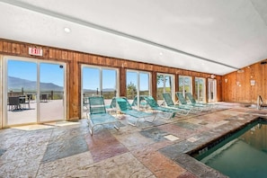 An indoor swimming pool with green lounge chairs and an exit sign.