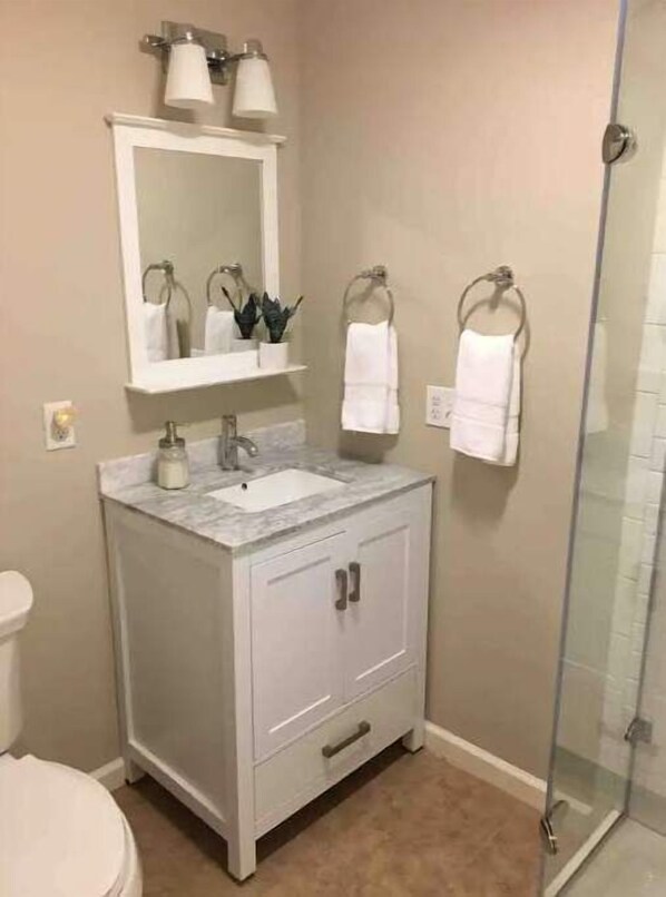 Un baño con tocador blanco, espejo, lavamanos y ducha.