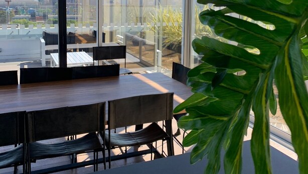 Ett modernt mötesrum med ett stort bord och stolar, stora fönster med utsikt över staden och ett tak med en träpaneldesign.