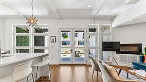 Uma cozinha moderna com bancada branca, banquetas e luminária pendente.