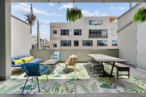 Un balcón al aire libre con sofá, sillas, una mesa y plantas colgantes.