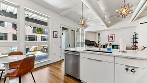 Cozinha moderna com armários brancos, lava-louças e um espaço de refeições com mesa e cadeiras.