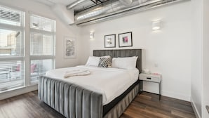 A modern bedroom with a large bed, a nightstand, and a window with blinds. - Art District Dream | RiNo Art Lofts (Denver)