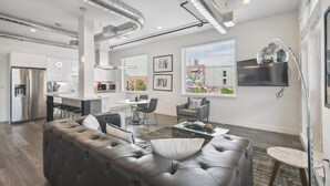 A modern living room with a leather sofa, dining area, kitchen, and large windows. - Art District Dream | RiNo Art Lofts (Denver)