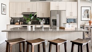 Une cuisine moderne avec des meubles en bois clair, un comptoir en granit, des appareils en acier inoxydable et un îlot central doté de tabourets de bar.