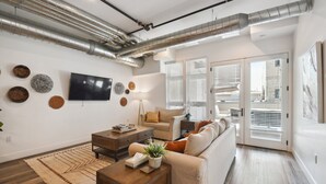 A modern living room with a sofa, coffee table, and TV. There are decorative wall pieces and a plant on the coffee table. - Brushed & Bold | RiNo Art Lofts (Denver)