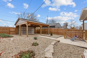 Un jardin avec une terrasse couverte, une clôture en bois et un espace recouvert de gravier.