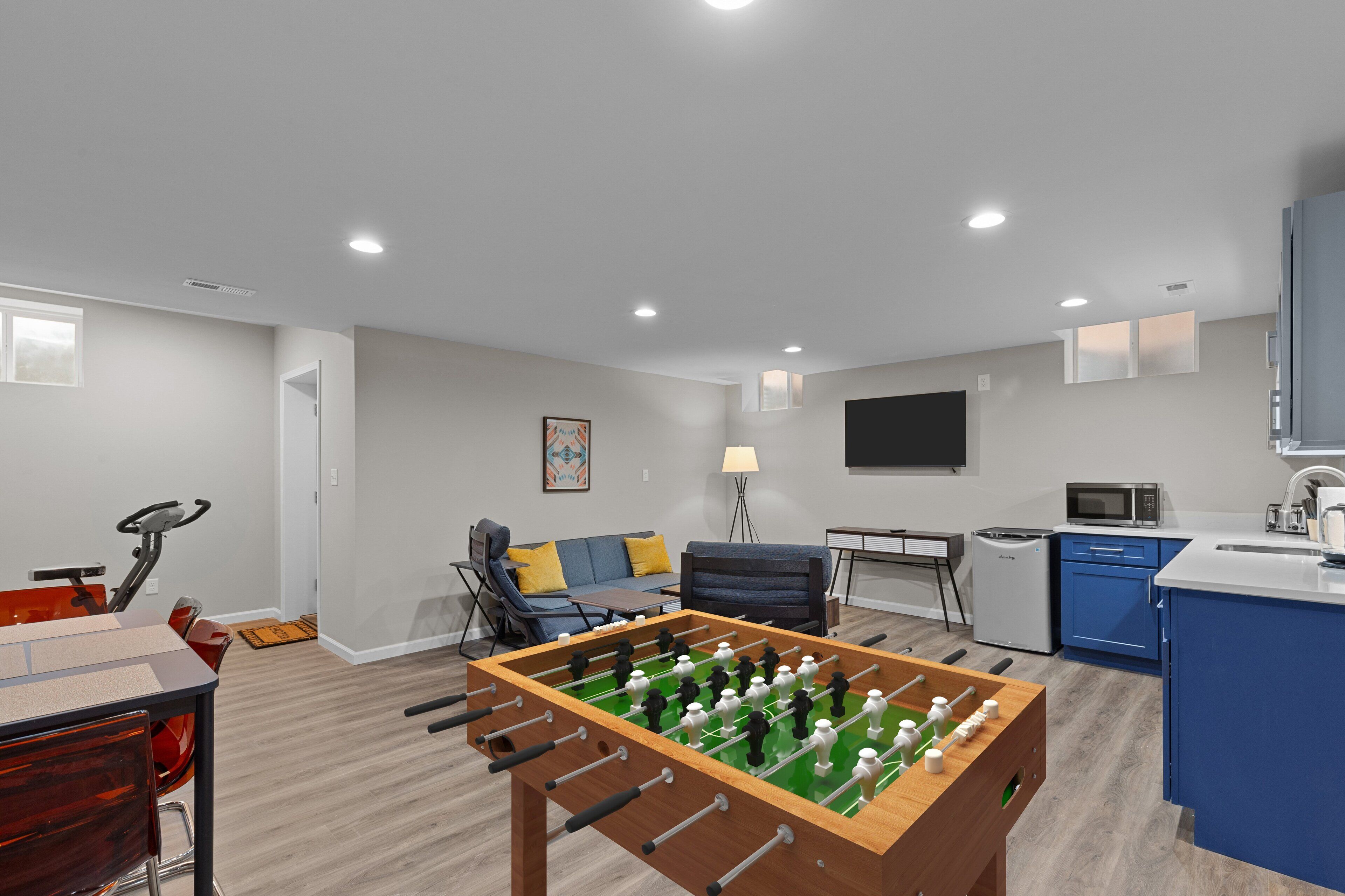 A modern living room with a foosball table, a sofa, a coffee table, and a TV.