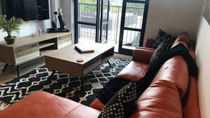 A modern living room with a leather sofa, a coffee table, and a TV. - Funky Fitzroy 2 bedroom Apartment in Old Chocolate Factory (Fitzroy)