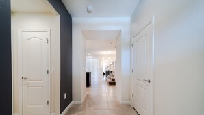 Un couloir avec des portes blanches, un sol carrelé de couleur beige et un escalier en arrière-plan.