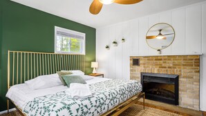Ein Schlafzimmer mit einem Bett, einem Holzkopfteil, einem Kamin, einem Deckenventilator und einem Fenster mit Jalousien.