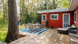 Eine Holzterrasse mit Gartenmöbeln, einem Grill und einem kleinen roten Gebäude mit Fenstern.