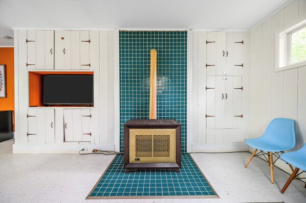 Une pièce dotée d’un poêle à bois encastré, de meubles blancs et d’une chaise bleue.