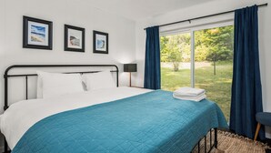 A bedroom with a bed, a window with curtains, and three framed pictures on the wall.