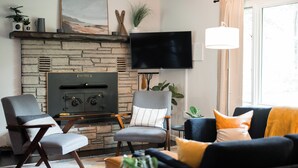 A living room with a stone fireplace, a flat-screen TV mounted on the wall, and a comfortable seating area with a sofa and armchairs.