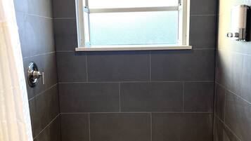 Una ducha con ventana, azulejos oscuros y suelo de mosaicos hexagonales.