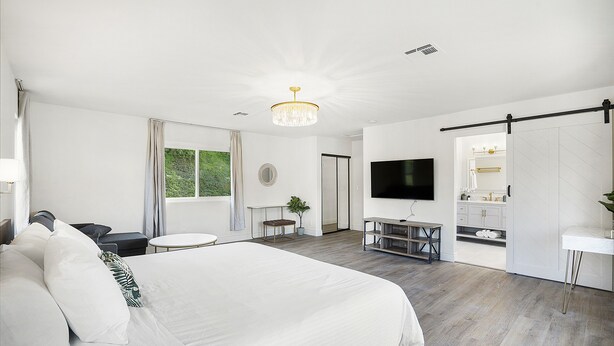 A modern hotel room with a large bed, a TV, a desk, and a bathroom visible through an open door. - Family Haven: Sports court/ Game Room/ King Beds (La Mesa)