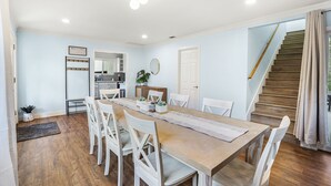A dining area with a wooden table, white chairs, a rug, a welcome sign, a mirror, and a staircase leading to another level. - Family Haven: Sports court/ Game Room/ King Beds (La Mesa)