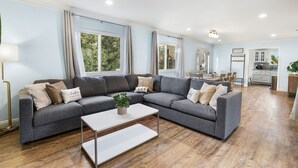 A modern living room with a grey sectional sofa, a white coffee table, and a kitchen in the background. - Family Haven: Sports court/ Game Room/ King Beds (La Mesa)