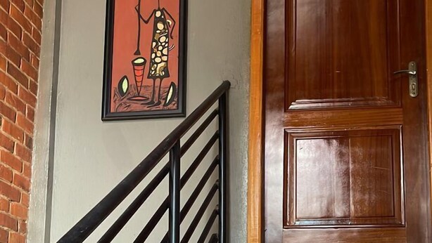 A staircase with wooden steps and black metal railings, leading to a wooden door with a brass handle. - Cozy Bricks Apartments (Mile 11)