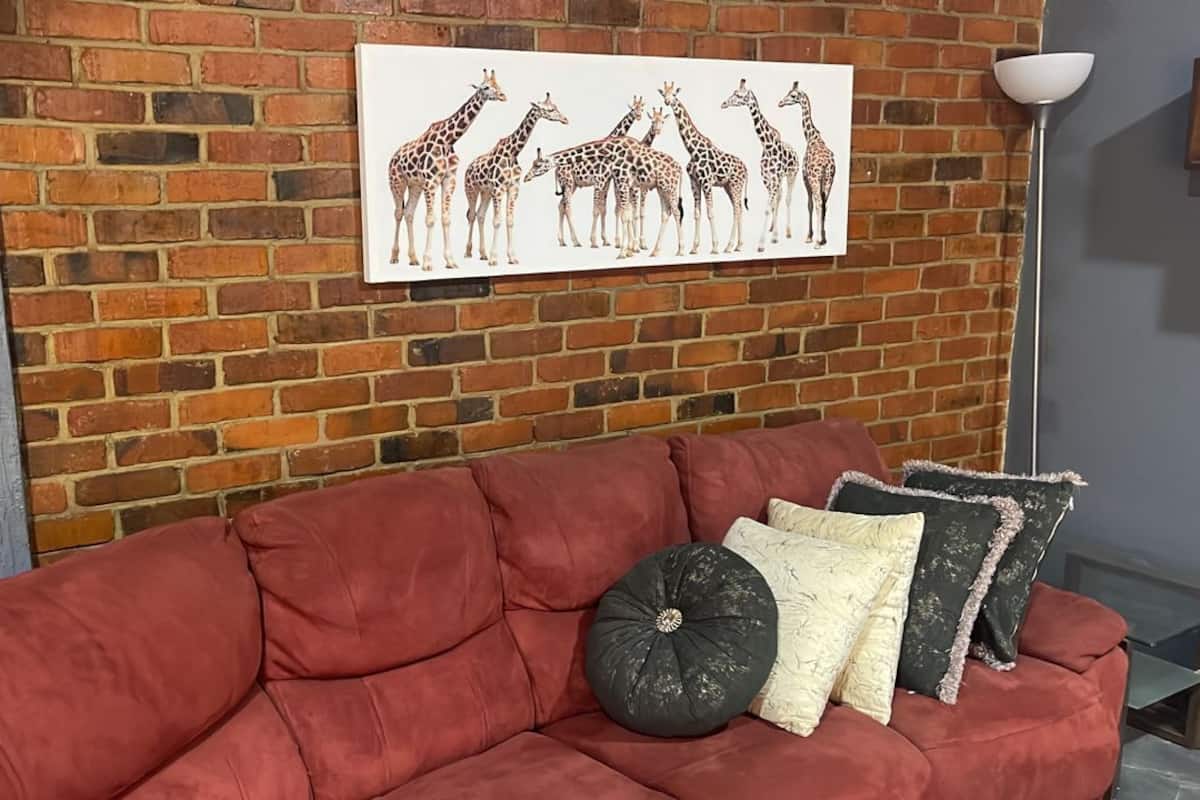 A red sofa with decorative pillows against a brick wall with a giraffe artwork.