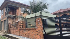 A two-story house with a brick exterior, a balcony, and a gated entrance. - Cozy Bricks Apartments (Mile 11)
