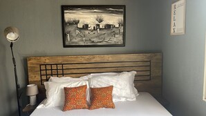 A bedroom with a wooden headboard, white bedding, and two patterned pillows. - Cozy Bricks Apartments (Mile 11)