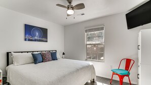 A bedroom with a bed, a ceiling fan, a window, a red chair, and a TV mounted on the wall. - Strip View! Retreat 4 Mi to Silver Dollar City (Branson)