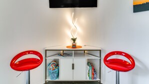 A room with two red bar stools, a white cabinet with a plant, and a flat-screen TV mounted on the wall. - Strip View! Retreat 4 Mi to Silver Dollar City (Branson)
