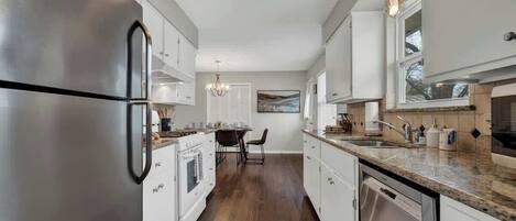 A modern kitchen with stainless steel appliances, white cabinetry, and a granite countertop.