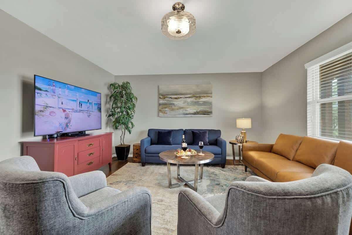 A living room with a flat-screen TV, a blue sofa, a brown sofa, and grey armchairs.