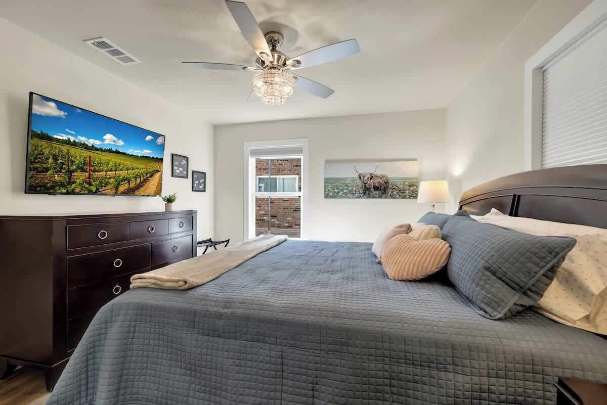Ein Schlafzimmer mit einem großen Bett, einem Deckenventilator, einem Fernseher an der Wand und Blick auf einen Weinberg.