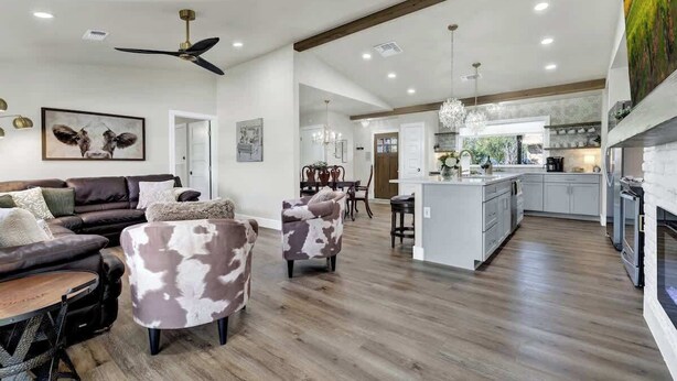 A spacious living room with a dark brown leather sofa, a white coffee table, and a patterned armchair. A ceiling fan and pendant lights are visible. - Crystal Cow Haus! (Fredericksburg)