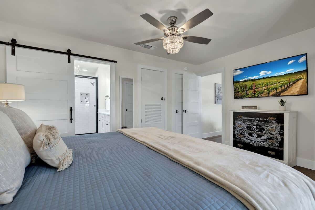A bedroom with a bed, a ceiling fan, a TV, and a fireplace.